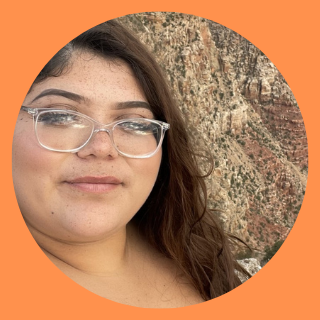 Female with glasses standing in front of mountain.